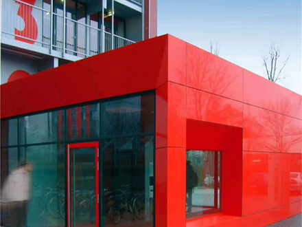 Red aluminium composite panel volume wrapping the ground floor of a mixed-use building