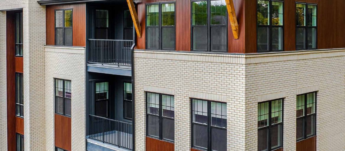 Three-storey mixed-use building clad in FastPlank woodgrain aluminium plank siding between fields of white brick